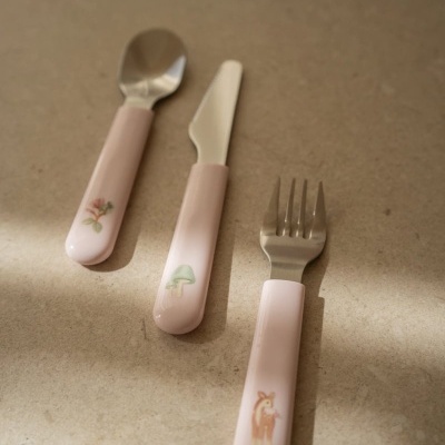Talheres infantis com cabo rosa claro e desenhos decorativos sobre superfície bege
