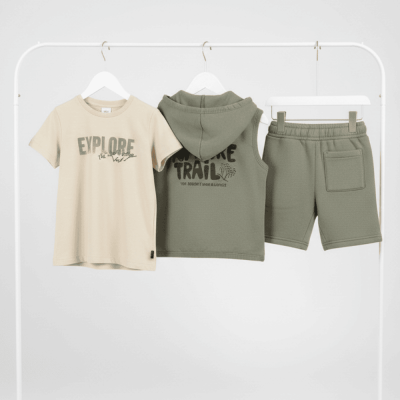 Conjunto de roupa infantil com t-shirt bege, colete com capuz e calções verdes pendurados em cabides