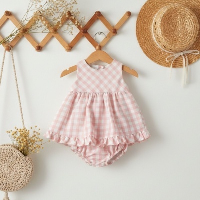 Vestido de bebé rosa e branco xadrez com folhos pendurado em cabide em parede branca com decoração