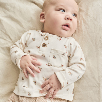 Bebé deitado com roupa creme e bege com padrões pequenos de cão e detalhes de botão de madeira.