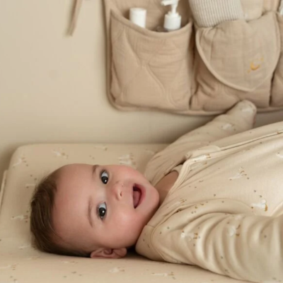 Bebé deitado em colchão e pijama bege com estampas pequenas, organizador bege com frascos em segundo plano.