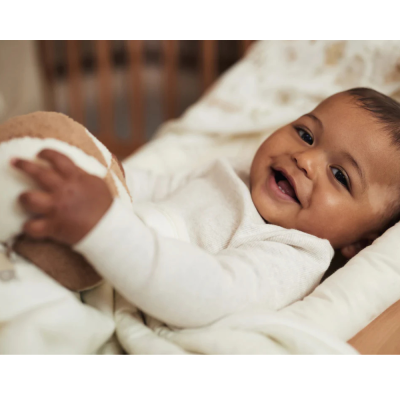 Bebé sorridente deitado segurando bola de peluche castanha e branca