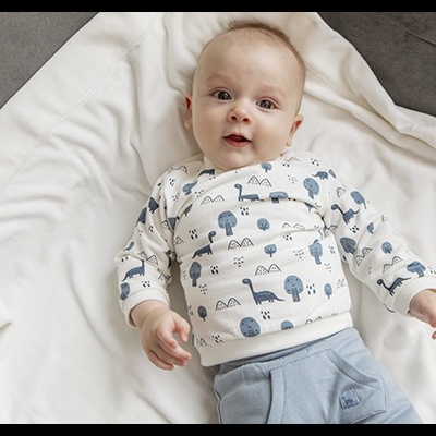 Bebé deitado com roupa azul e branca e manta branca num sofá cinzento