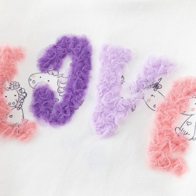 Palavra LOVE em tule colorido sobre tecido branco com desenhos de personagens.