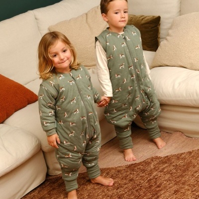 Crianças em pijamas verdes com padrão de cães numa sala com sofá e tapete