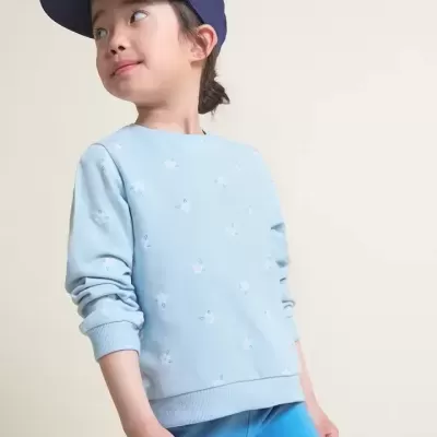 Criança com roupa desportiva azul e boné azul escuro em fundo bege