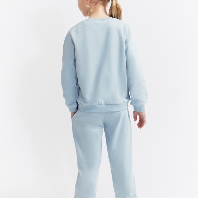 Criança de costas com conjunto desportivo azul claro e ténis brancos