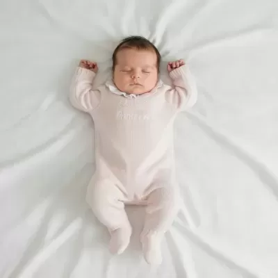 Bebé a dormir com macacão cor-de-rosa claro e gola branca com folhos
