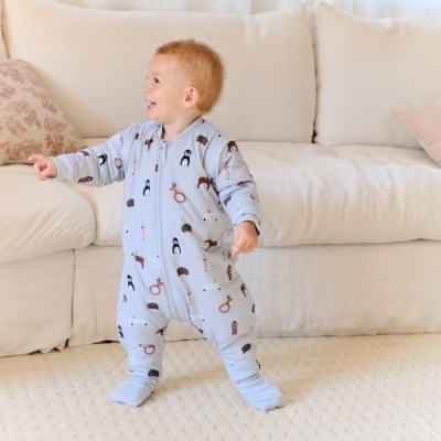 Criança com pijama azul claro de animais, em sala com sofá branco