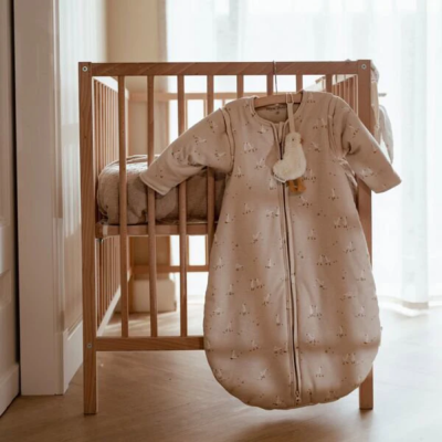Saco de dormir bege com padrão pendurado em berço de madeira