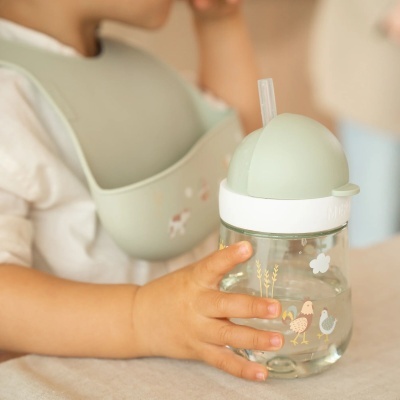 Copo infantil com tampa verde e desenho de galinhas segurado por criança com babete verde.
