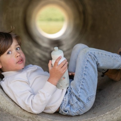 Criança deitada dentro de um tubo de cimento segurando uma garrafa branca