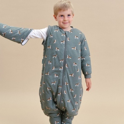 Menino com pijama acolchoado verde com padrão de cães, em fundo bege