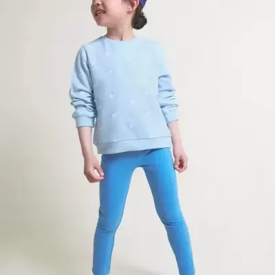 Criança com casaco azul claro e leggings azuis e boné azul escuro