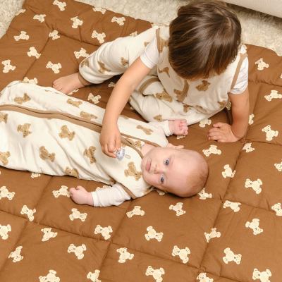 Tapete castanho com ursinhos, duas crianças a brincar, bebé e menino, ambiente interior