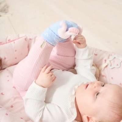 Bebé deitada em almofada rosa com meias azuis decoradas com elefantes cor-de-rosa