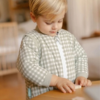 Bebé a usar macacão xadrez bege e branco a brincar com peças de madeira