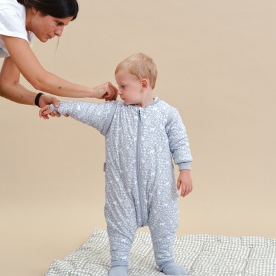 Menino com fato de pijama azul claro e branco em tapete xadrez a ser ajudado por mulher com camiseta branca