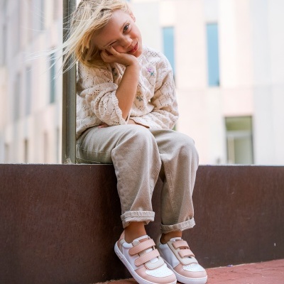 Criança loira sentada com roupa casual e sapatilhas brancas e rosa ao ar livre