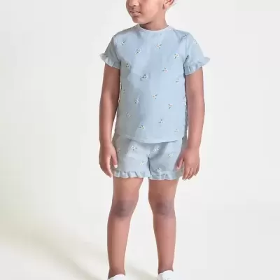 Criança vestindo conjunto azul com padrões de flores e ténis brancos