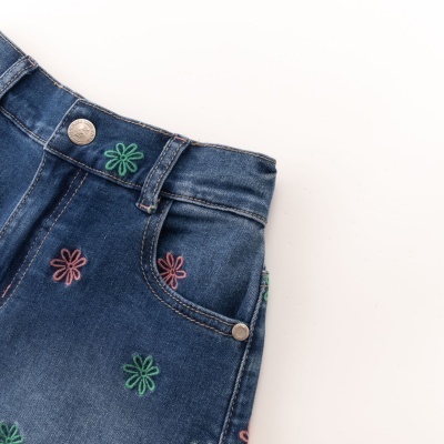 Calças de ganga com bordados de flores verdes e rosas, botão metálico e costuras visíveis.