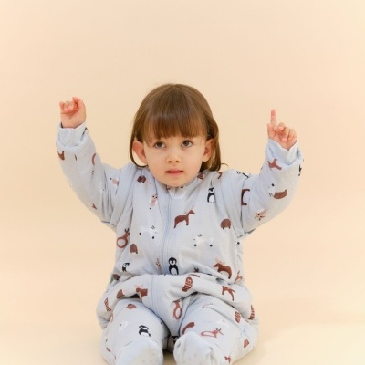 Bebé com pijama azul claro com padrões de animais sentado em fundo bege