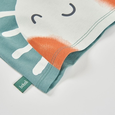 Pano branco com estampado de girafa em verde azulado e laranja com etiqueta verde boboli.