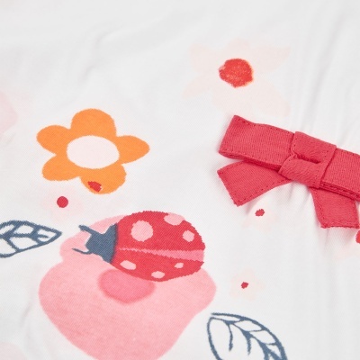 tecido branco com estampado de flores e joaninha e laço vermelho