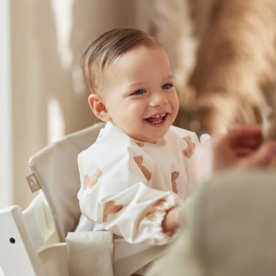 Bebé na cadeira alta vestido com babete branco com ossos castanhos