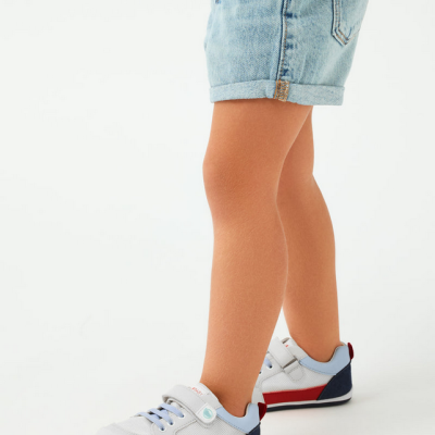 Sapatilhas infantis coloridas com velcro e atacadores, usadas por criança com calções de ganga.