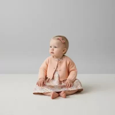 Bebé com cardigan cor de pêssego e vestido floral sentada