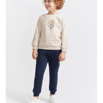 Camisola bege com estampado de foguete e texto 'SPACE IS THE PLACE' usada por criança com calças azuis e ténis brancos