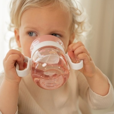 Criança a beber de copo infantil rosado com pegas brancas