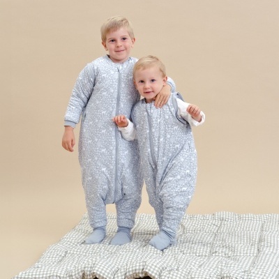 Duas crianças com sacos de dormir cinza claro com desenhos brancos em colchonete xadrez bege claro