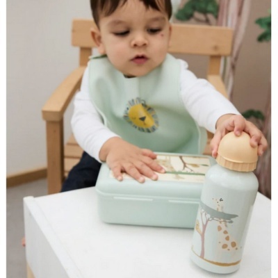 Criança com babete verde água, caixa de almoço e garrafa com desenhos de animais.