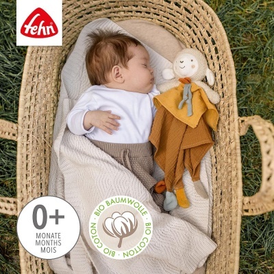 Bebé a dormir numa cesta com brinquedo de pano em tons de mostarda e laranja.