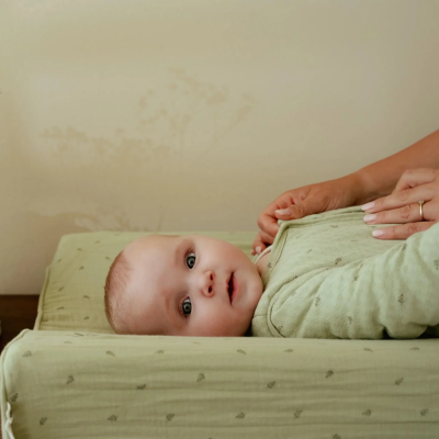 Bebé deitado de roupa verde claro com padrão subtil e mãos a ajustar a roupa.