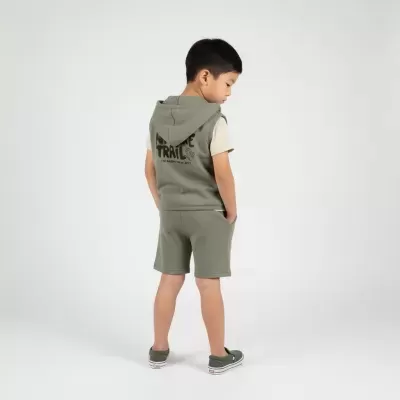 Criança com colete de capuz e calções verdes e ténis verdes em fundo branco