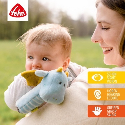 Bebé com brinquedo de pelúcia azul com asas amarelas ao colo de mulher sorridente ao ar livre.