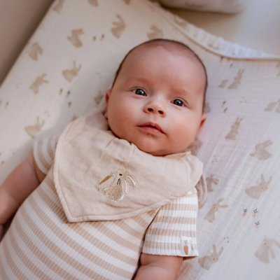Bebé deitado com macacão às riscas bege e branco e babete bege bordado com coelho