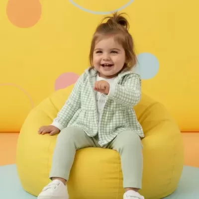 Criança sentada numa poltrona amarela redonda com fundo amarelo e círculos coloridos