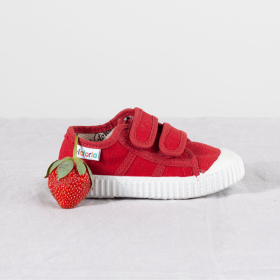 Ténis infantil vermelho com sola branca e fecho velcro, acompanhado por um morango