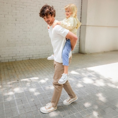 Homem com criança às costas numa parede branca de tijolos