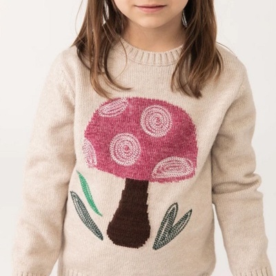 Camisola bege com padrão de cogumelo e folhas verdes, criança a usar.