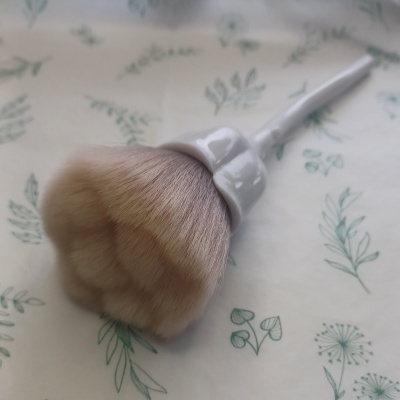 Pincel de maquilhagem branco com cerdas macias em fundo com padrão de folhas verdes