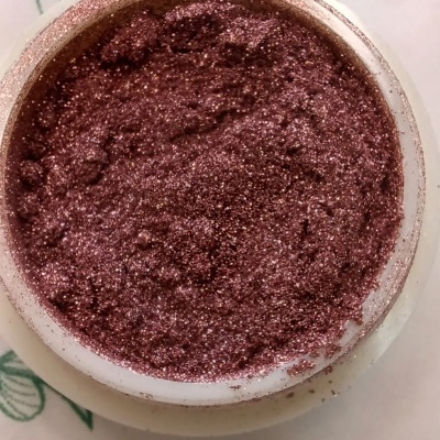 Recipiente com pó cremado castanho brilhante sobre superfície branca com folhas verdes.