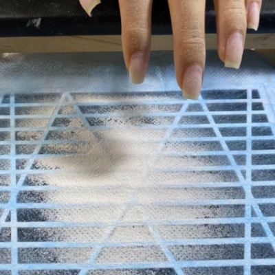 Mão com unhas longas naturais sobre grelha azul com pó branco