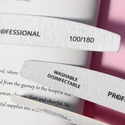 Três lixas de unhas cinza claro com texto escrito preto sobre uma página de livro