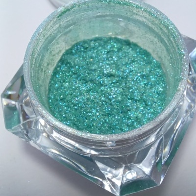 Frasco transparente com glitter verde-azulado brilhante e tampa aberta.