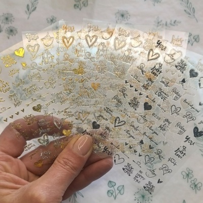 Folhas transparentes com autocolantes metálicos coloridos com corações, estrelas e palavras em inglês.